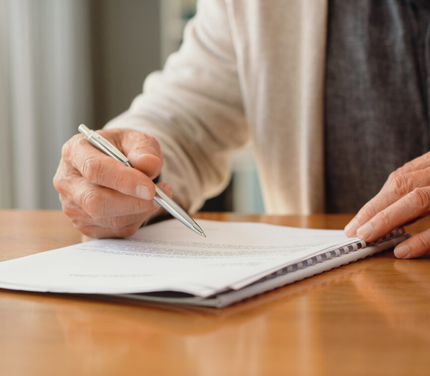 Hands of pension man reading retirement paperwork about policy, investment options and funeral cover while planning finance, insurance and budget at home. Signing will, legal document and contract