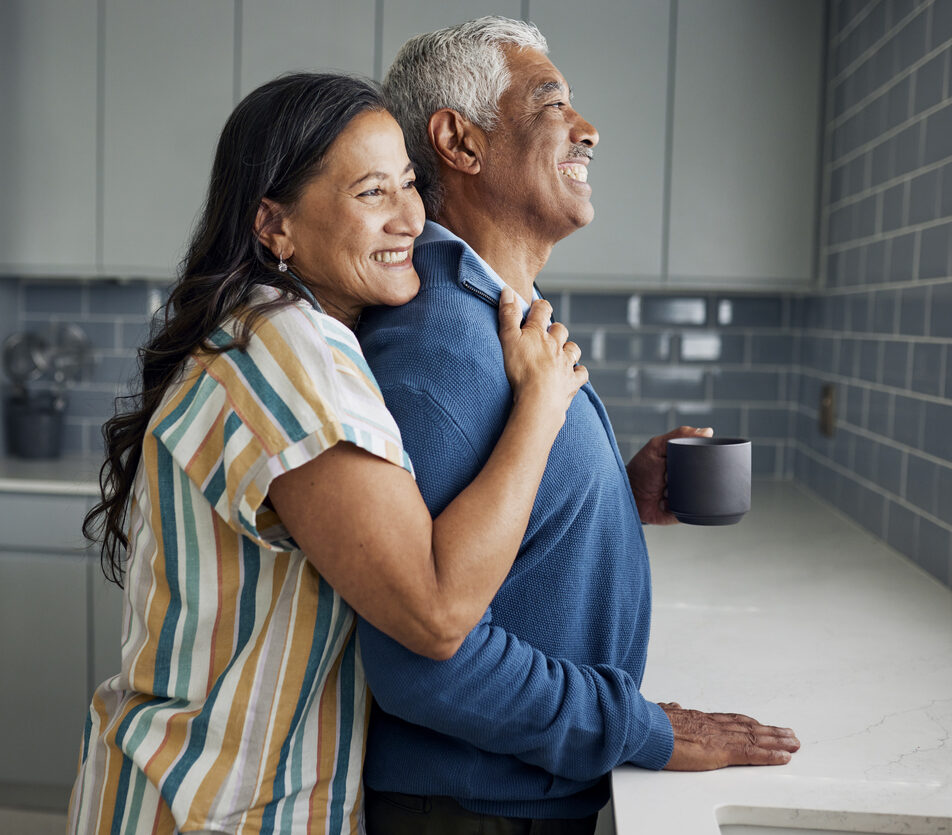 An elderly couple is drinking coffee and gazing out the kitchen window.
