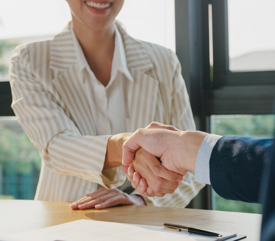Closeup of young Asian businessman sign a contract investment professional document agreement and shake hands at office. Businesspeople in workplace concept.