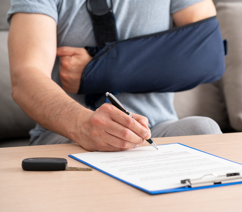 Close up of a man hands with broken arm signing insurance document after car accident at home