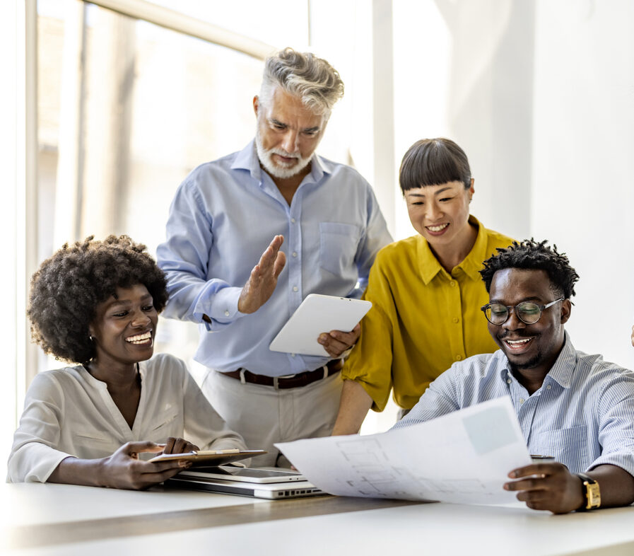 A diverse group of professionals collaborating around a table in a modern office. They are discussing documents with positivity and teamwork. The atmosphere is productive and inclusive, emphasizing collaboration.