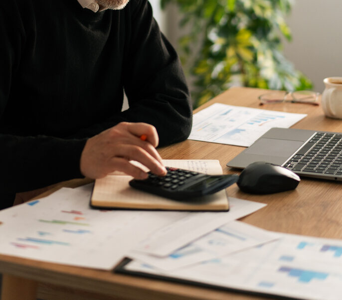 Senior adult man calculating financial documents with a calculator and laptop in a modern office setting