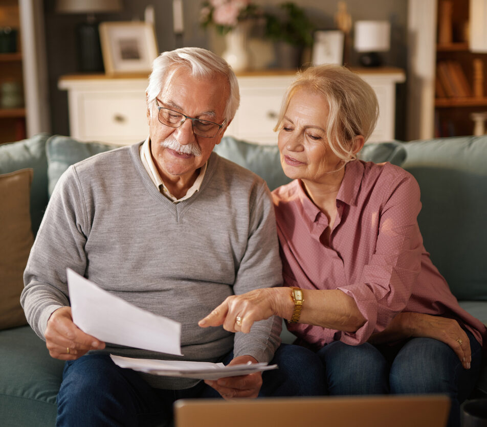 Elderly couple reviewing life insurance policy documents, planning their future finances together on the sofa