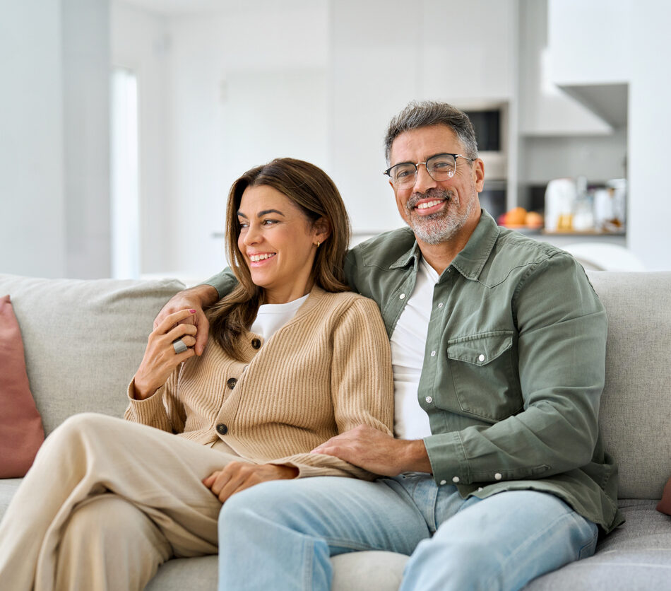 Happy middle aged mature romantic couple in their 40s hugging sitting on couch at home. Smiling older man and woman in love relaxing on sofa together enjoying chilling in modern house living room.